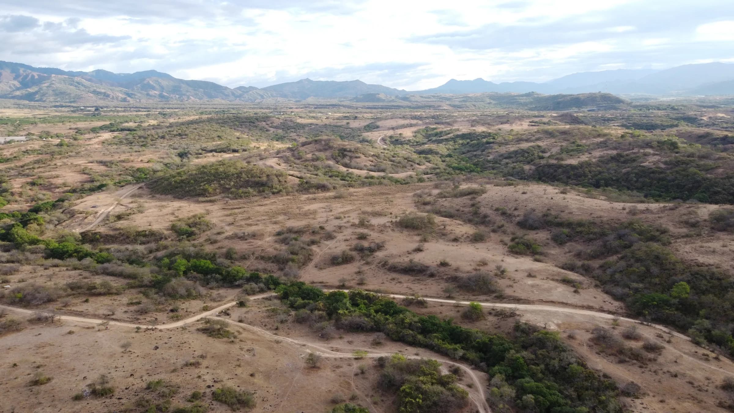 Vista aérea de caminos de tierra recorriendo el valle donde está el predio, con las montañas al fondo.