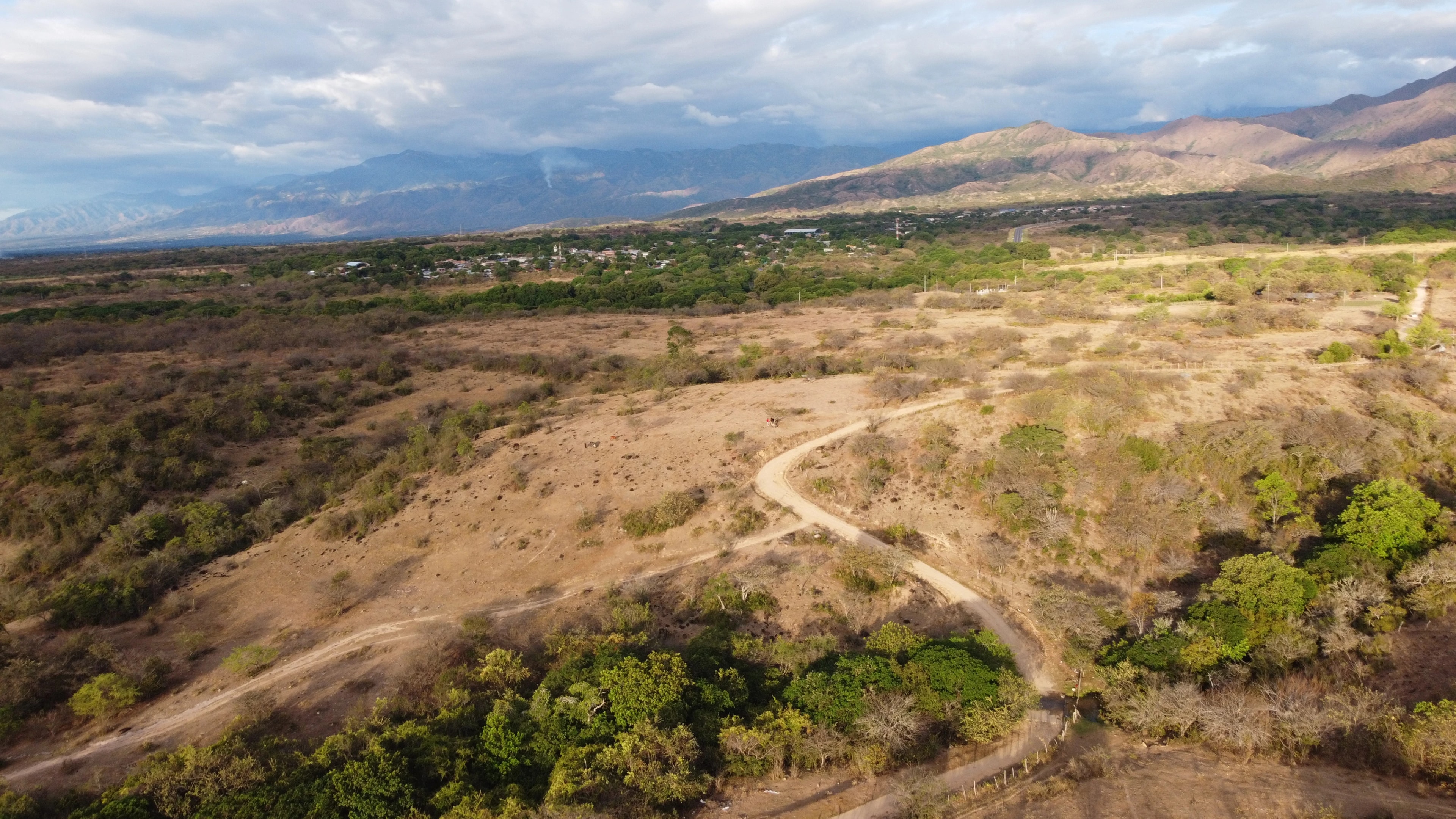 Vista aérea panorámica del valle de Campestre Los Cristales, con un camino de tierra cruzando el terreno y la cordillera al fondo.